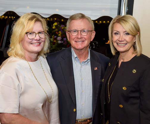 Three people smiling at the camera while at a formal event.